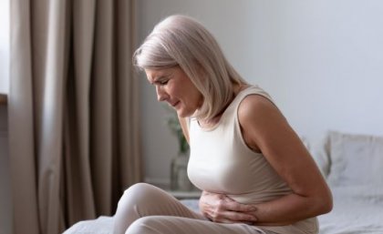 Endometriosis is a chronic and often debilitating inflammatory disease, affecting 1 in 7 Australian women. Image: Adobe. A woman in pain sitting on her bed clutching her stomach.